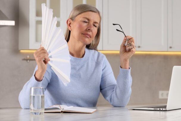 Vouw van middelbare leeftijd heeft een opvlieger en wappert met een waaier.