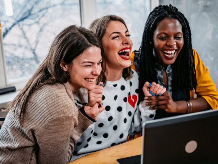 drie schaterlachende vrouwen achter een laptop