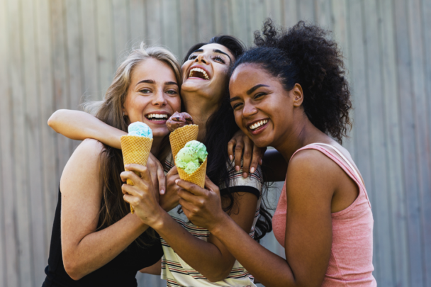 drie vrolijke vrouwen knuffelen elkaar en eten een ijsje|drie vriendinnen aan tafel