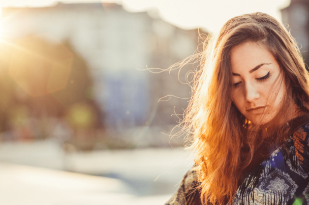 vrouw zit buiten in de zon en kijkt naar beneden|vrouw zit in de auto met zonnebril en kijkt gestresst