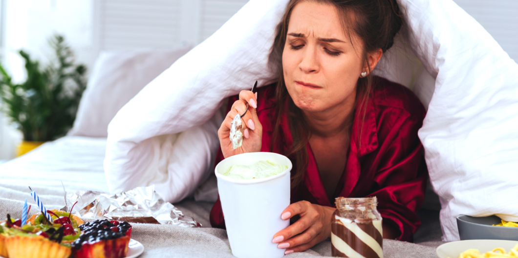 vrouw is emotioneel en eet ijs onder een dekbed|vrouw ligt somber op de bank te zappen