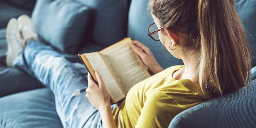 vrouw leest een boek op de bank|vrouw zit op stapel boeken en leest er een|vrouw zit op stapel boeken en leest er een