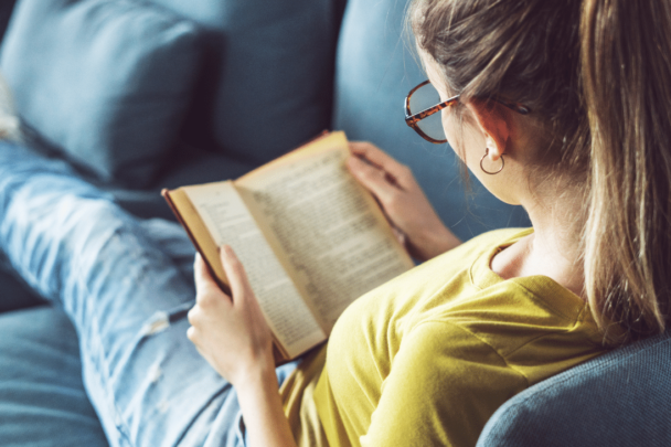 vrouw leest een boek op de bank|vrouw zit op stapel boeken en leest er een|vrouw zit op stapel boeken en leest er een