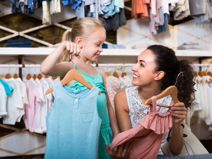 Klein meisje is met haar moeder in een kinderkledingwinkel. Samen bekijken ze kleding.