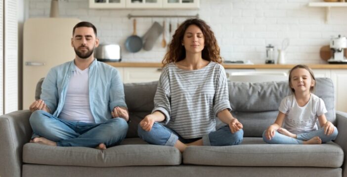 gezin van man vrouw en kind doet een meditatie op de bank