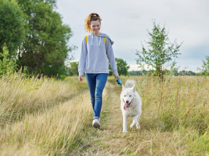 Vrouw laat hond uit in een bosrijk heidegebied.