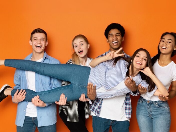 Vijf jongeren staan vrolijk samen op de foto op een oranje achtergrond.