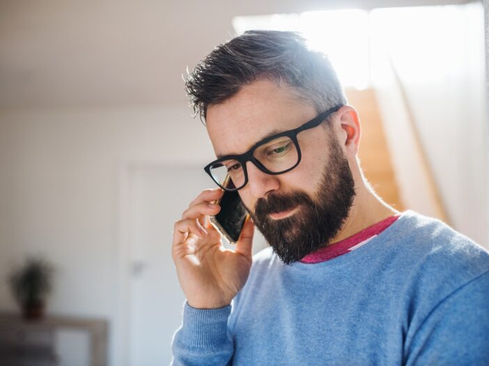 Man met blauwe trui en bril voert een telefoongesprek.