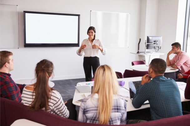 Groepje mensen luistert aandachtig naar een presentatie van een jonge vrouw.