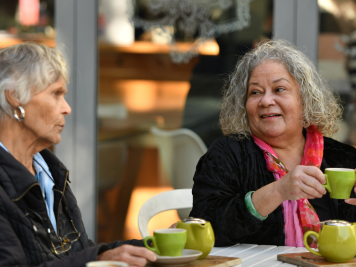 twee vrouwen met een kopje koffie die samen zitten te kletsen