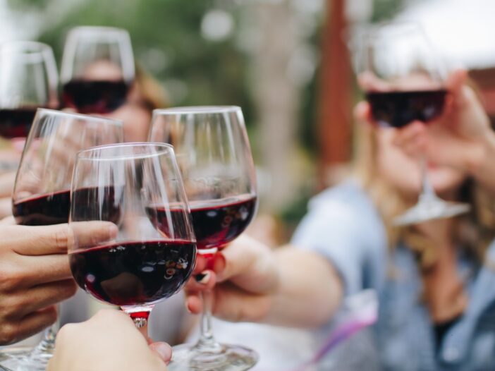 Groep mensen proost met een glas rode wijn.