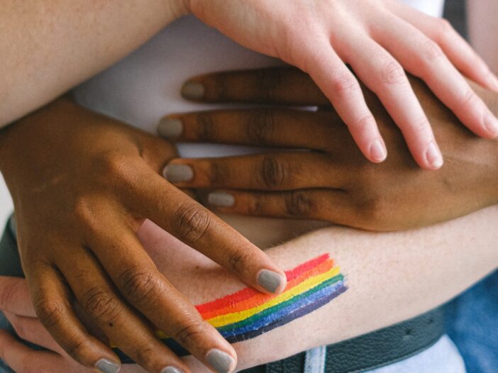 handen houden elkaar vast met in beeld een kleine regenboog vlag