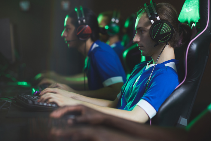 Verslaafde gamers met een headset op. Ze zitten in een donkerhol achter hun computer te gamen.