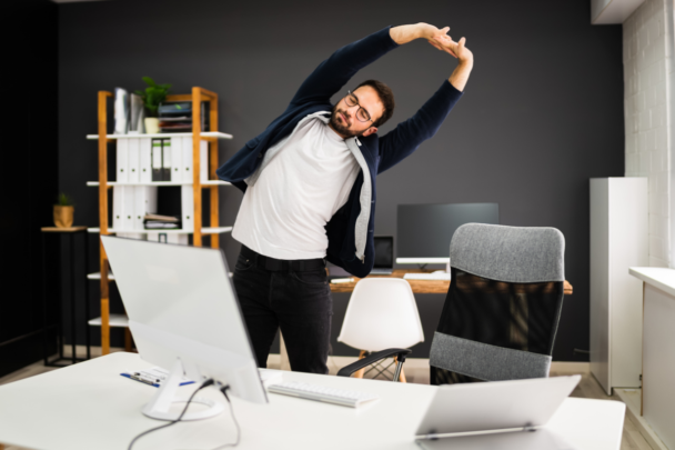 man doet beweegoefening achter zijn bureau