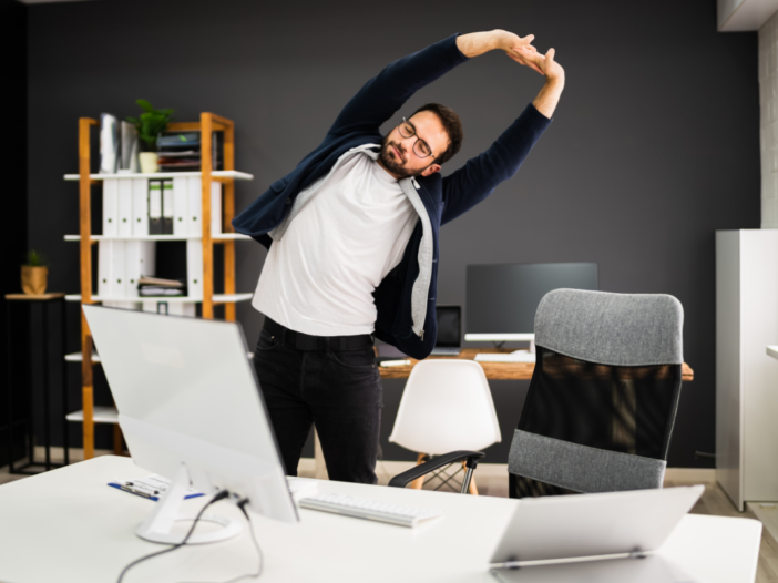 man doet beweegoefening achter zijn bureau