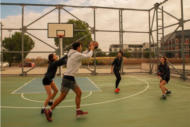 Vier jongeren spelen basketbal in een park.