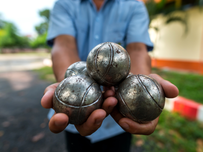 man houdt 3 jeu des boules ballen vast