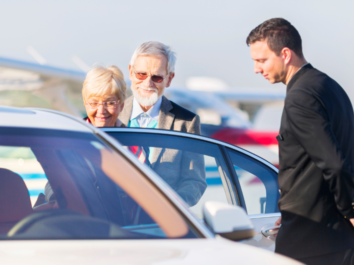 twee ouderen stappen in de auto bij een chauffeur