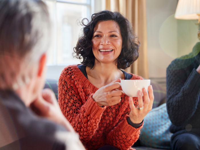 Drie mensen drinken samen een kopje koffie. De vrouw moet ook lachen daarbij.