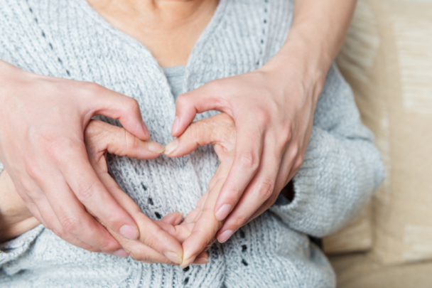 twee paar handen vormen een hart op de buik van een oudere vrouw