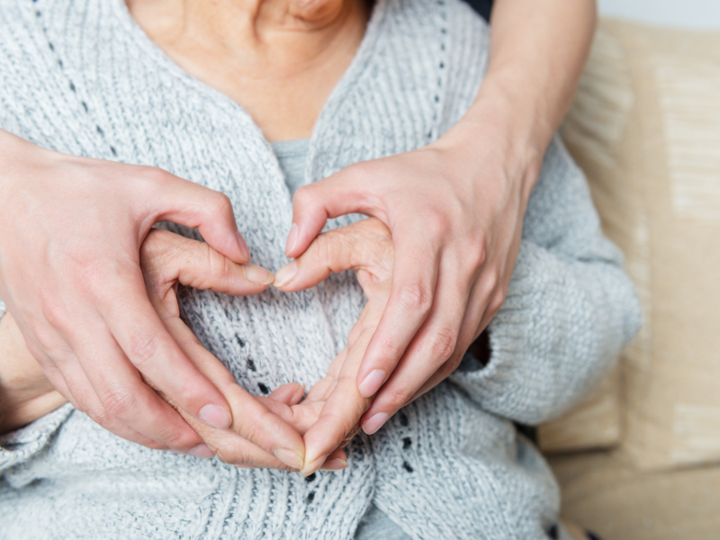 twee paar handen vormen een hart op de buik van een oudere vrouw