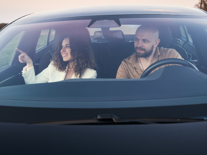 Twee mensen in een auto. Een man en een vrouw, ze lachen allebei terwijl ze naar hetzelfde kijken.