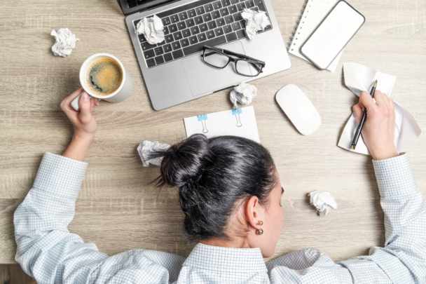 man zit gestresst achter zijn laptop, met koffie en verfrommelde papieren