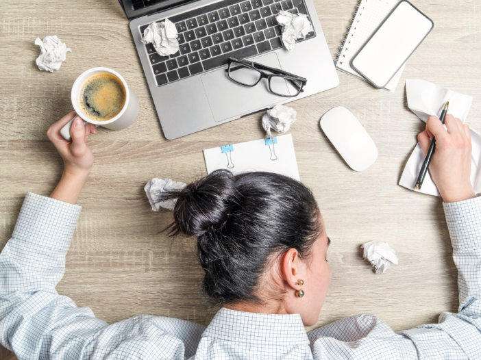 man zit gestresst achter zijn laptop, met koffie en verfrommelde papieren