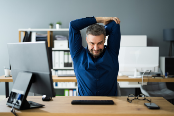 man stretcht zijn schouders terwijl hij aan een bureau zit