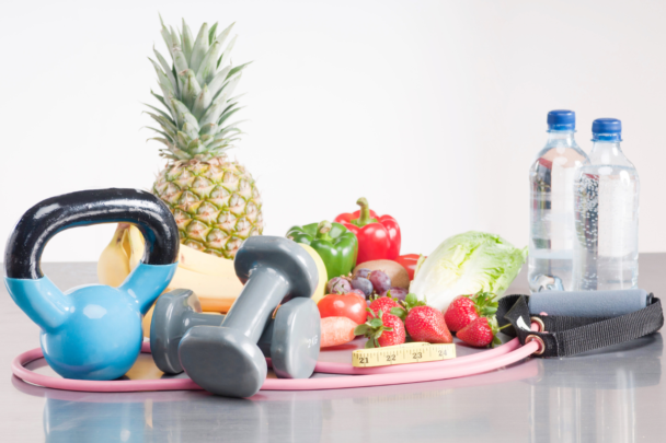 Tafel met daarop fruit, flesjes water, dumbbells en een kettlebell