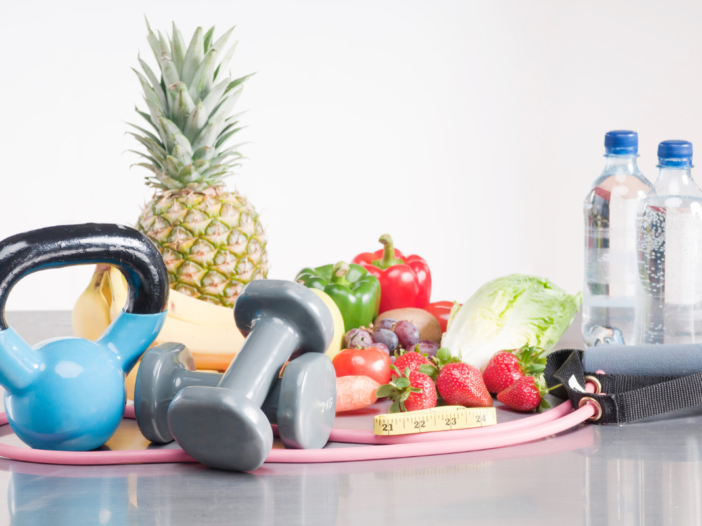 Tafel met daarop fruit, flesjes water, dumbbells en een kettlebell