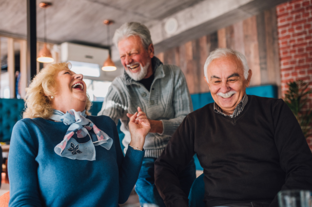 Ouderen die samen lachen. En twee van de drie ouderen houden elkaars hand vast.