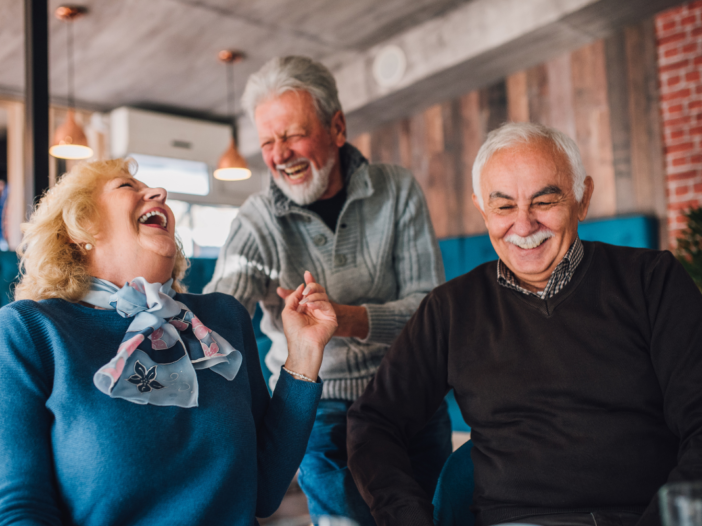 Ouderen die samen lachen. En twee van de drie ouderen houden elkaars hand vast.