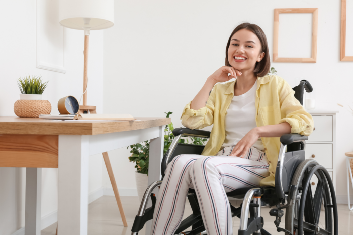Lachende vrouw in een rolstoel. Ze heeft een geel blousje aan en ze is thuis.