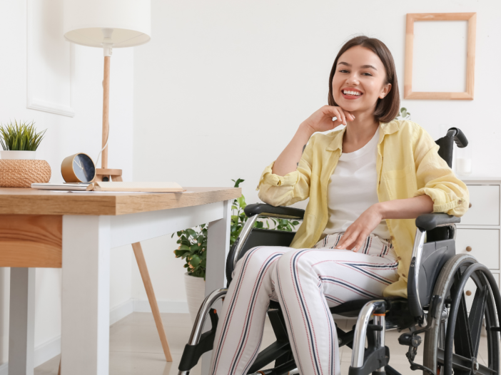 Lachende vrouw in een rolstoel. Ze heeft een geel blousje aan en ze is thuis.