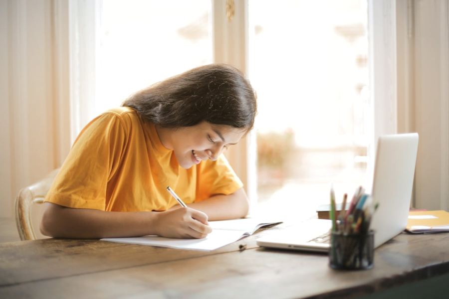 vrouw is aan het schrijven in een schrift. Ze zit aan tafel.