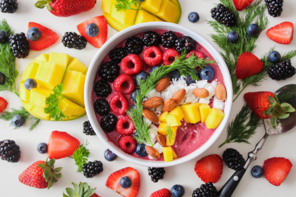 Een kom op tafel met verschillende soorten tropisch fruit. Zoals frambozen, aardbeien en mango.