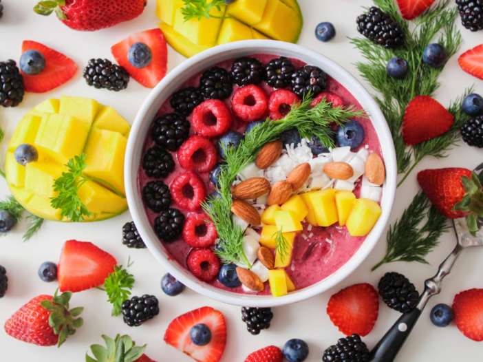 Een kom op tafel met verschillende soorten tropisch fruit. Zoals frambozen, aardbeien en mango.