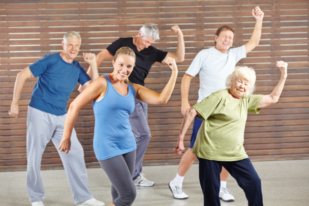 Een groep mensen die allemaal samen aan het dansen zijn. Ze hebben het naar hun zin en zijn tijdens het bewegen aan het lachen.