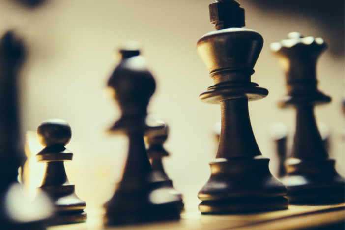 Een paar schaakpionnen die in het donker op een schaakbord staan. De koning staat voorop.