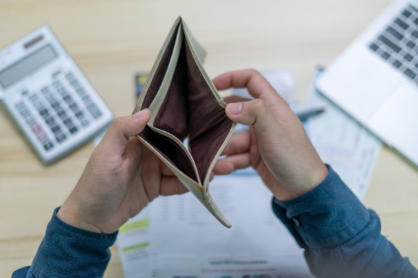 Een lege portemonnee met daarachter ook nog een rekenmachine en wat papierwerk. Dit doelt op iemand die geen inkomen heeft of in ieder geval geen geld meer heeft.