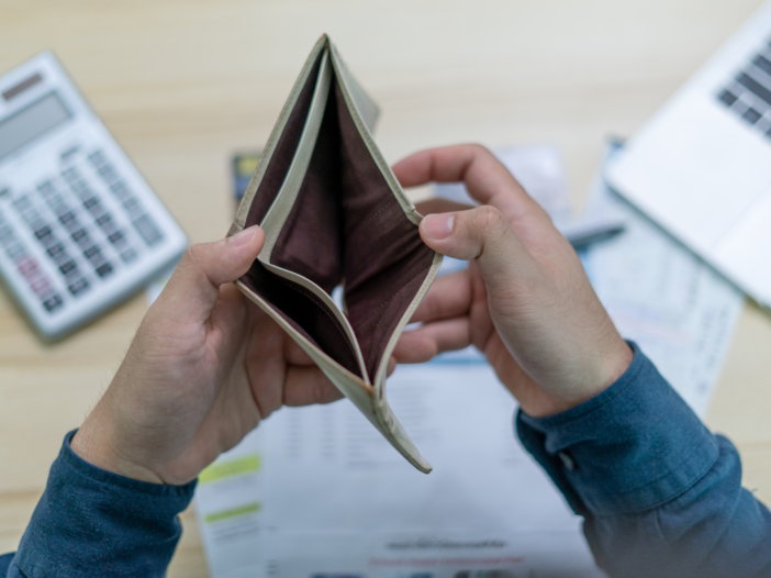 Een lege portemonnee met daarachter ook nog een rekenmachine en wat papierwerk. Dit doelt op iemand die geen inkomen heeft of in ieder geval geen geld meer heeft.