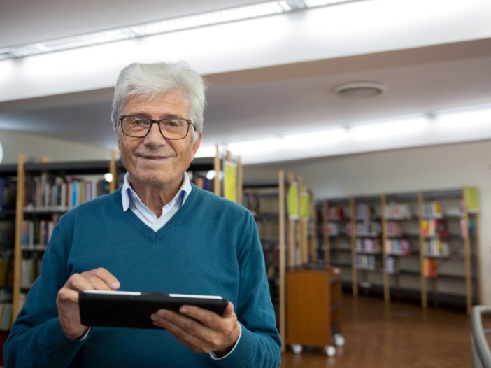 Man met grijze haren en een bril op lacht naar de camera. Hij is te vinden in de bibliotheek met een tablet in zijn handen om zo digitaler te worden,