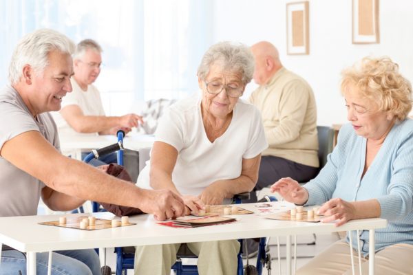 Drie personen van oudere leeftijd zitten aan tafel. Ze spelen een spel.