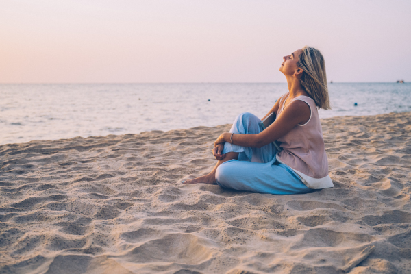 vrouw zit op het strand te genieten van de zonsondergang