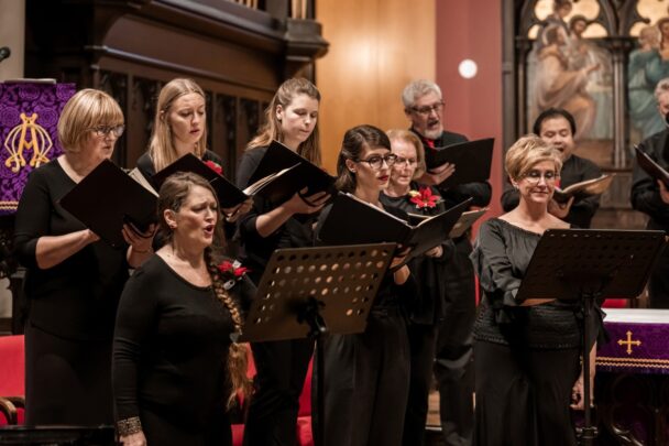 In dit koor staan mannen en vrouwen te zingen uit volle borst. Ze hebben allemaal zwarte kleren aan en staan in een kerk.