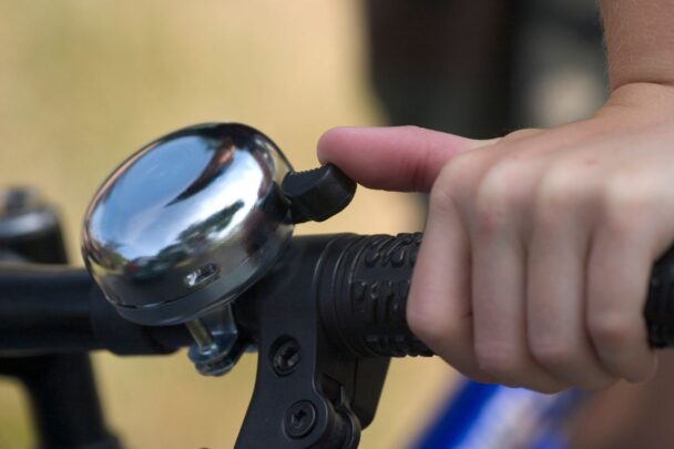 Een hand belt met een fietsbel op een fiets.