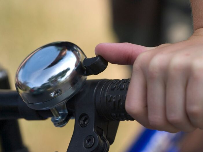 Een hand belt met een fietsbel op een fiets.