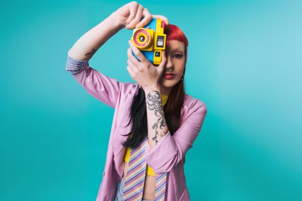 Vrouw met rood haar in een kleurrijke outfit maakt een foto richting de kijker