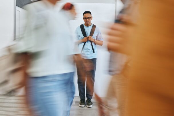 Man staat met zijn tas helemaal alleen op de wereld lijkt het. Alle mensen lopen deze man straal voorbij.